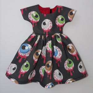 May include: A black dress with a pattern of colorful eyeballs with red dripping blood. The dress has short sleeves and a round neckline.
