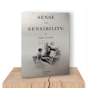 May include: A vintage book cover for "Sense and Sensibility" by Jane Austen. The cover features a black and white illustration of two women playing a piano in a room with a window and a framed picture on the wall. The text on the cover reads "Sense and Sensibility: By Jane Austen. London 1811."