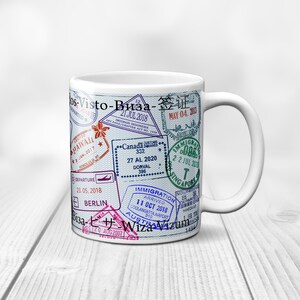 May include: White ceramic mug with a design of various passport stamps from different countries, including Hawaii, Canada, Singapore, and Berlin. The text "Visto-Bиза-签证" is printed on the mug.