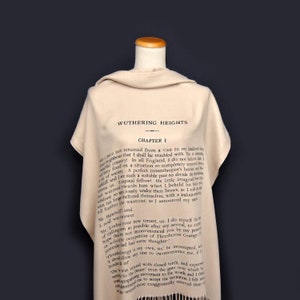 May include: A beige scarf with a black print of the first chapter of the book "Wuthering Heights" by Emily Bront&euml;. The text includes the title of the book, the chapter number, and the first paragraph of the book.