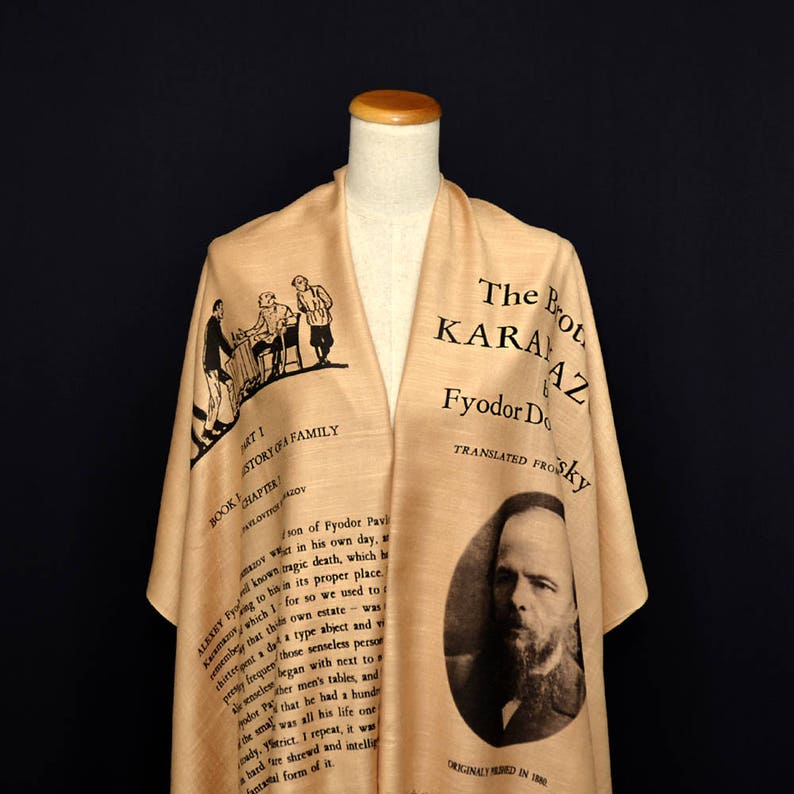 May include: A beige scarf with black text and illustrations. The text reads "The Brothers Karamazov" by Fyodor Dostoevsky, translated from the Russian by Constance Garnett. The scarf also features a black and white illustration of Fyodor Dostoevsky.