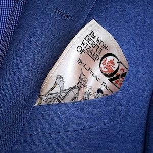May include: A white pocket square with a vintage illustration of the Tin Man from "The Wonderful Wizard of Oz" by L. Frank Baum. The pocket square is folded and placed in the pocket of a blue blazer.