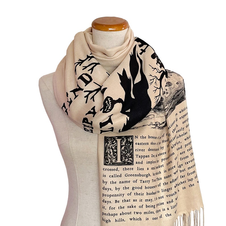 May include: A beige scarf with a black and white illustration of a tree and text that reads "N the bosom of Hudson's river, there lies a small town, which is called Greensburgh, by the name of Tarry Town, which is named for the propensity of their husbands to linger about two miles, but mere days, by the good houses of the adjacent far from it, for the sake of being wise and perhaps about two miles, there is a little high hills, which is one of the"