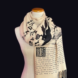 May include: A beige scarf with a black and white print of a tree and a bird. The scarf has text printed on it that reads "N the bosse of th eastern shure Huds river dead by laciefcholas Tappan shere of alert, whil and impii Prondion are tol crossed, there lies et town of from th by the name of Tarry his name webut merri is called Greensburgh both is more ze taven Propensity of their hushto linger abther lap of days, by the good houser of the adiar far from days. Be that as it may not vouch it, for the sake of beine Rise and s Perhaps about two miles is a lice high hills, which is one of the"