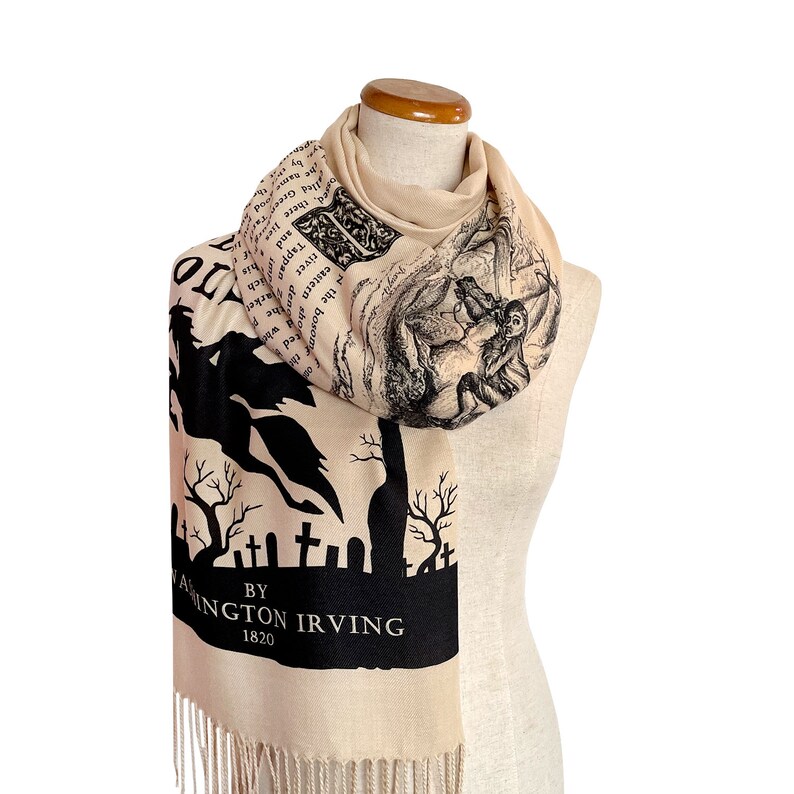 May include: A beige scarf with black text and illustrations. The text reads "BY WASHINGTON IRVING 1820" and includes an excerpt from "The Legend of Sleepy Hollow". The scarf features a black silhouette of a headless horseman riding a horse.