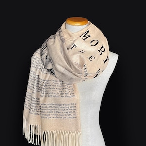May include: A beige scarf with black text and a graphic print of a man's face. The text on the scarf reads "Moby Dick" and "Herman Melville".