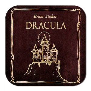 May include: Square coaster with a dark burgundy background and a gold border. The coaster features the title "DR&Aacute;CULA" in gold lettering, with the author's name, "Bram Stoker," above. A gold illustration of a castle is also present.
