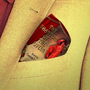 May include: A yellow blazer with a book titled "The Phantom of the Opera" tucked into the pocket. The book cover features a red background with gold lettering and an illustration of a masked figure in a red cloak.