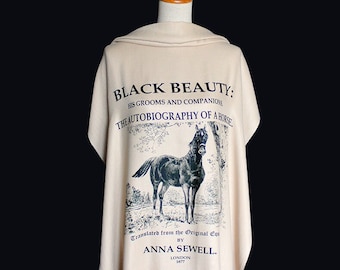 May include: A beige scarf with a black and white illustration of a horse and the text "BLACK BEAUTY: HIS GROOMS AND COMPANIONS THE AUTOBIOGRAPHY OF A HORSE Translated from the Original Equ BY ANNA SEWELL. LONDON 1877"