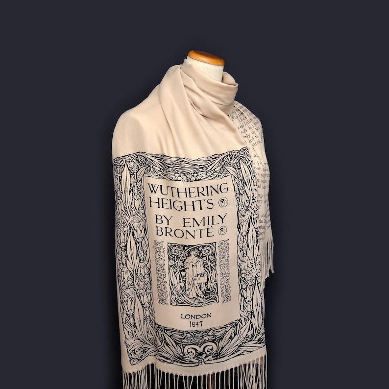 May include: A cream-colored scarf with a black and white print of the book cover for "Wuthering Heights" by Emily Bront&euml;. The print includes the title, author, and publication date of 1847. The scarf has fringe on the bottom.