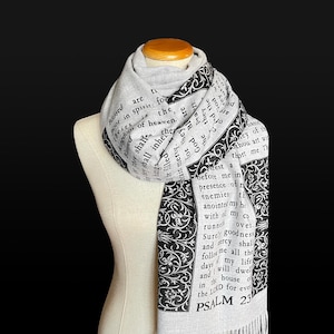 May include: A light gray scarf with black text and decorative borders. The scarf features text from Psalm 23. The scarf is draped over a mannequin and has a fringed edge.
