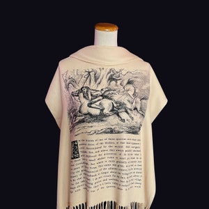 May include: A beige shawl featuring a black and white illustration of a person riding a horse through a forest. The text "N the bosom of one of those spacious com which ind eastern shore of the Hudson, at that boni expusine river denominated by the ancient Dut navigate Tappan Zee, and where they always prally shortened and implored the protection of St.  small market town of rural pouch by And Green but which is moet rallyly it came of My Town. This name wat given wand is forme there lin Prasity when onmarke the the good ousewine of the adiacent country metal of bande to linger about the villag that way. I do not vouch for the fact frest in coketing precise and authest Norfor village Nits there is a little withered among for the Maps about that" is printed on the shawl.