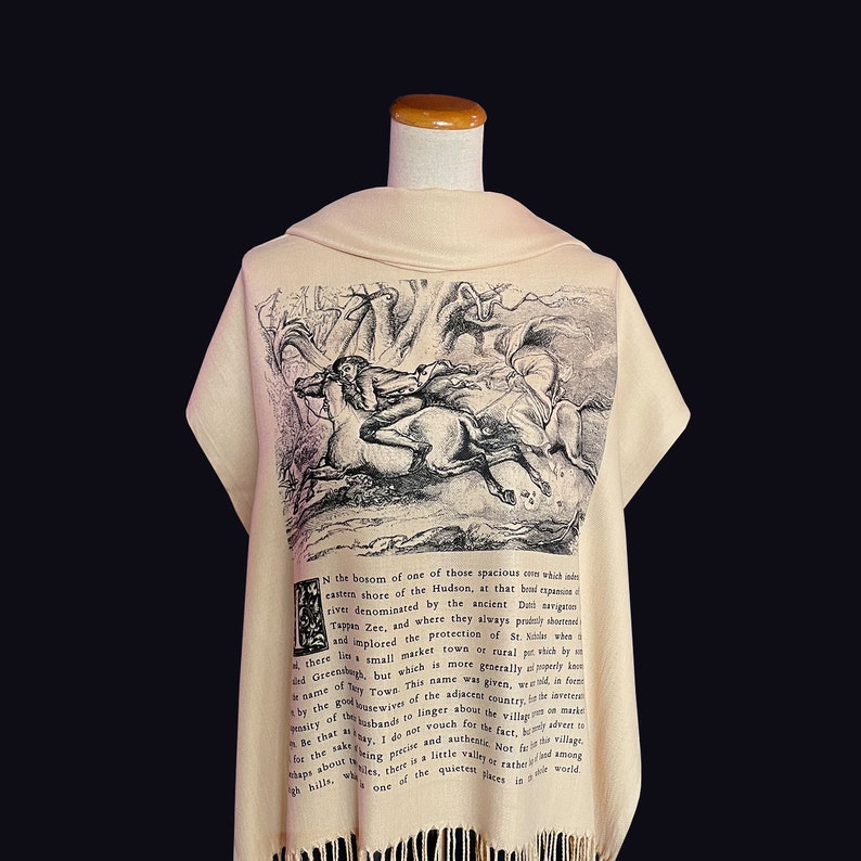 May include: A beige shawl featuring a black and white illustration of a person riding a horse through a forest. The text "N the bosom of one of those spacious com which ind eastern shore of the Hudson, at that boni expusine river denominated by the ancient Dut navigate Tappan Zee, and where they always prally shortened and implored the protection of St.  small market town of rural pouch by And Green but which is moet rallyly it came of My Town. This name wat given wand is forme there lin Prasity when onmarke the the good ousewine of the adiacent country metal of bande to linger about the villag that way. I do not vouch for the fact frest in coketing precise and authest Norfor village Nits there is a little withered among for the Maps about that" is printed on the shawl.