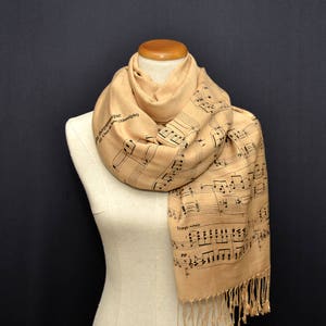 May include: A beige scarf with a musical note pattern and black fringe. The scarf has the text "Tempo rubato" and "pp" printed on it.