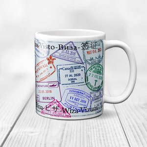 May include: White ceramic mug with a design of various colorful passport stamps from different countries, including Hawaii, Canada, Berlin, Australia, and Singapore. The stamps feature dates, locations, and immigration information.