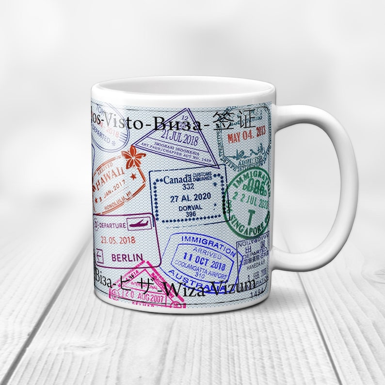 May include: White ceramic mug with a design of various colorful passport stamps from different countries, including Hawaii, Canada, Berlin, Australia, and Singapore. The stamps feature dates, locations, and immigration information.