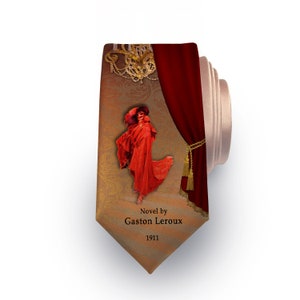 May include: A brown and gold tie with a red curtain and a woman in a red dress. The tie has the text "Novel by Gaston Leroux 1911" printed on it.