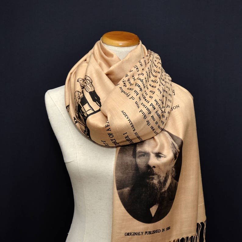 May include: A tan silk scarf with a black and white print of a portrait of Fyodor Dostoevsky and text from his novel "The Brothers Karamazov". The text reads "ORIGINALLY PUBLISHED IN 1880".
