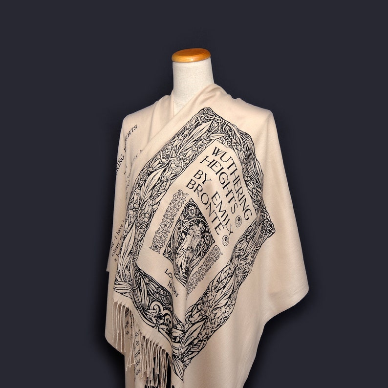 May include: A cream-colored shawl with a black and white print of the book cover for "Wuthering Heights" by Emily Bronte. The shawl has fringe on the bottom.