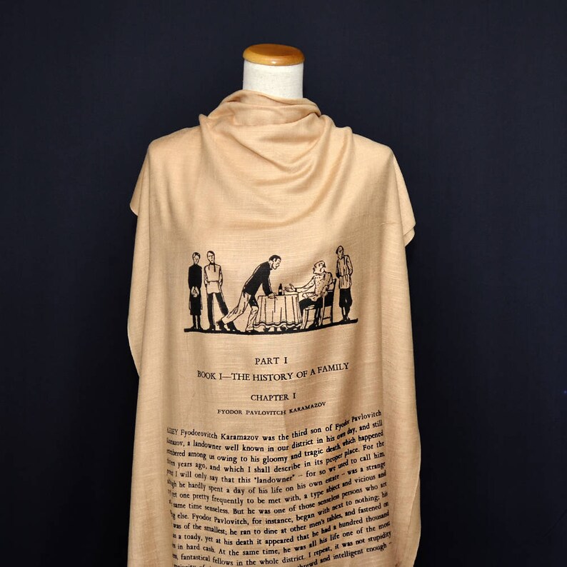 May include: A beige silk scarf with a black and white illustration of a scene from the book "The Brothers Karamazov" by Fyodor Dostoevsky. The text on the scarf reads "Part I, Book I - The History of a Family, Chapter I, Fyodor Pavlovitch Karamazov".