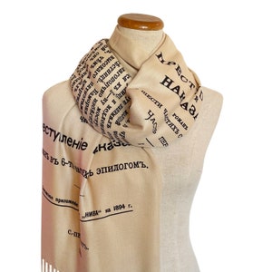 May include: A beige scarf with black text that reads "НАЧАЛО" and "ПРЕСТУПЛЕНІЕ" in Cyrillic script. The scarf is folded and draped over a mannequin.