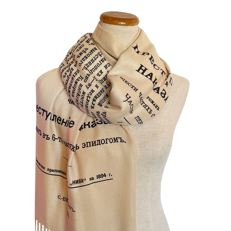 May include: A beige scarf with black text that reads "НАЧАЛО" and "ПРЕСТУПЛЕНІЕ" in Cyrillic script. The scarf is folded and draped over a mannequin.