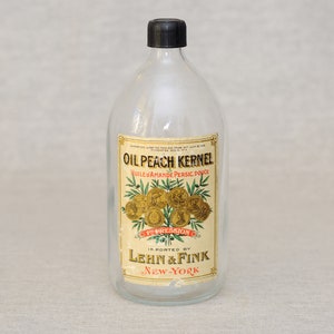 Puede incluir: Una botella de vidrio transparente con una tapa negra y una etiqueta que dice "Oil Peach Kernel, Huile d'Amande Persic Douce, Pression a, Importado por Lehn & Fink, New-York".