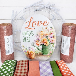 May include: An oval sign with the text Love Grows Here, a floral arrangement, and a green watering can, positioned in front of a white wire wreath frame, flanked by two rolls of copper fabric mesh and six assorted patterned ribbons.