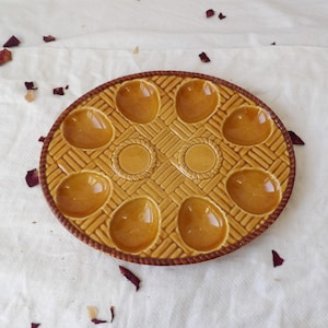 Peut inclure: Une assiette à escargots ronde en céramique beige avec huit cavités en forme d'escargot et deux puits centraux circulaires. L'assiette présente un motif de panier tressé et un bord tressé marron foncé. Diamètre d'environ 23 cm.