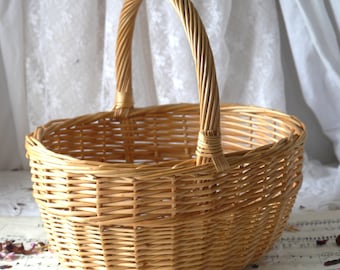 May include: A natural woven wicker basket with a single handle. The basket is oval shaped and has a light brown color.