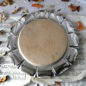 May include: A silver serving tray with a scalloped edge and a wooden centre. The tray is sitting on a piece of sheet music.