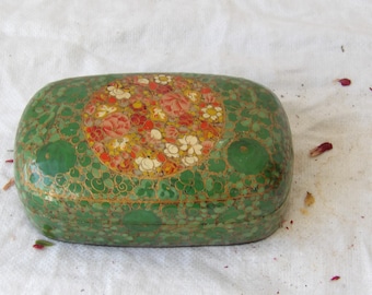 May include: A green, rectangular box with a floral design. The box has a central circular pattern of red, pink, yellow, and white flowers. The box is decorated with gold accents and a textured surface.