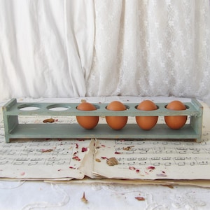 May include: A light blue wooden egg holder with four brown eggs inside. The holder is sitting on a sheet of music with dried flower petals.