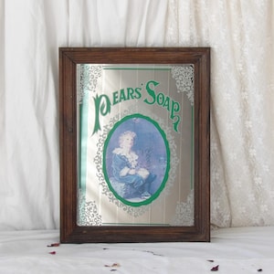 Op de afbeelding: Vintage spiegel met een donkerhouten frame en de groene tekst "Pears Soap". In het midden een ovaal portret van een kind in blauwe kleding, omringd door een groene rand en decoratieve elementen. Een klassiek reclame-object.