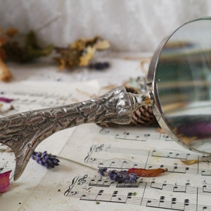 Peut inclure: Une loupe argent&eacute;e avec une poign&eacute;e textur&eacute;e en forme de branche d'arbre. La loupe est pos&eacute;e sur une feuille de musique avec des fleurs violettes.