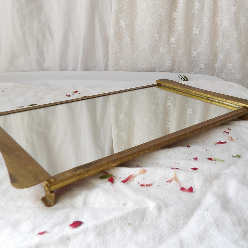 May include: A rectangular vanity mirror with a gold-colored frame. The mirror is set on a white surface with scattered red petals. The frame has a simple, elegant design.