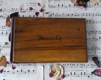 May include: A wooden box with a dark brown finish and the word "Nazareth" inscribed on the front. The box is resting on a sheet of music with floral accents.