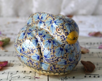 May include: A blue and gold papier-mâché bunny shaped box with a floral pattern. The bunny has a yellow nose and black whiskers.