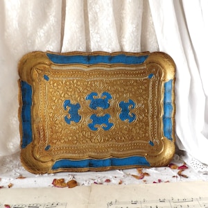 Può includere: Un vassoio decorativo dorato e blu con un design ornamentale. Il vassoio ha un bordo rialzato e un bordo blu.