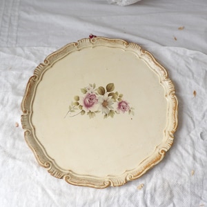 May include: Cream-coloured, scalloped-edge serving tray with a floral design. The tray features a painted bouquet of pink roses and white daisies. The rim has a distressed, gold-toned finish, adding a vintage aesthetic.