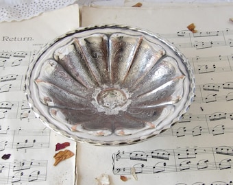 May include: A silver-plated bowl with an ornate design. The bowl has a scalloped edge and a raised center. The bowl is sitting on a sheet of music.