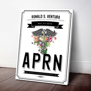May include: A white canvas print with black text that reads "Ronald S. Ventura - Advanced Practice Registered Nurse - May 21, 2019 - United States of America - APRN - University of Michigan School of Nursing". A black and white medical symbol with a snake wrapped around a staff is surrounded by colorful flowers.