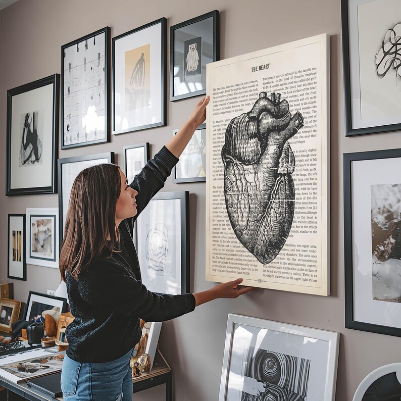 May include: A black and white anatomical illustration of the human heart with text about the heart. The illustration is printed on a white background and framed in a black frame. The image is hanging on a wall with other framed artwork.