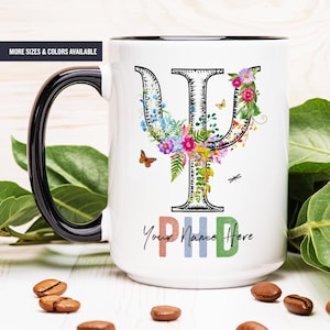 May include: White ceramic mug with a black rim and handle. The mug features a black and white outline of the Greek letter Psi, decorated with colorful flowers and butterflies. The text "Your Name Here" is printed below the Psi symbol in rainbow colors.