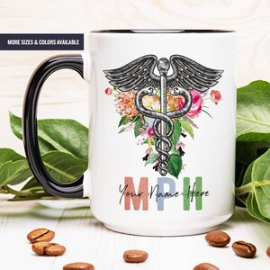 May include: White ceramic mug with a black handle. The mug features a black and white medical caduceus symbol surrounded by colorful flowers. The text "Your Name Here" is printed below the symbol in colorful letters.