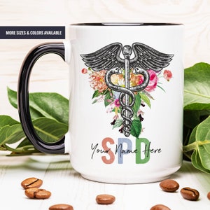 May include: White ceramic mug with a black rim and handle. The mug features a black and white medical caduceus symbol surrounded by colorful flowers. The text "Your Name Here" is printed below the symbol in rainbow colors.