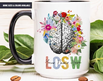 May include: White ceramic mug with a black handle. The mug features a colorful floral design surrounding a black and white anatomical brain illustration. The text "Your Name Here" is printed in colorful letters below the brain.