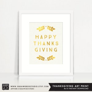 Può includere: Stampa in foglia d'oro con il testo "HAPPY THANKSGIVING" in una cornice bianca. La stampa presenta rametti dorati in alto e in basso al testo.