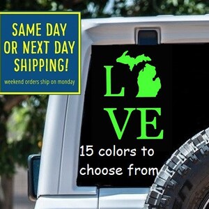 May include: A green vinyl decal with the word "LOVE" and an outline of the state of Michigan. The decal is attached to the back of a white Jeep. The text "15 colors to choose from" is also visible on the decal.