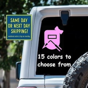 May include: A pink welding helmet sticker with a bow on top. The sticker is on the back of a white Jeep. The text "15 colors to choose from" is below the sticker.